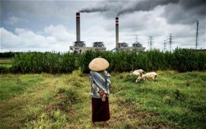 woman in a field walking towards a coal power plant