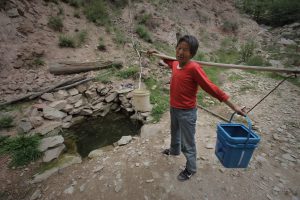 A woman collects water from a spring in a valley outside her village of Houjialiang in northwestern China