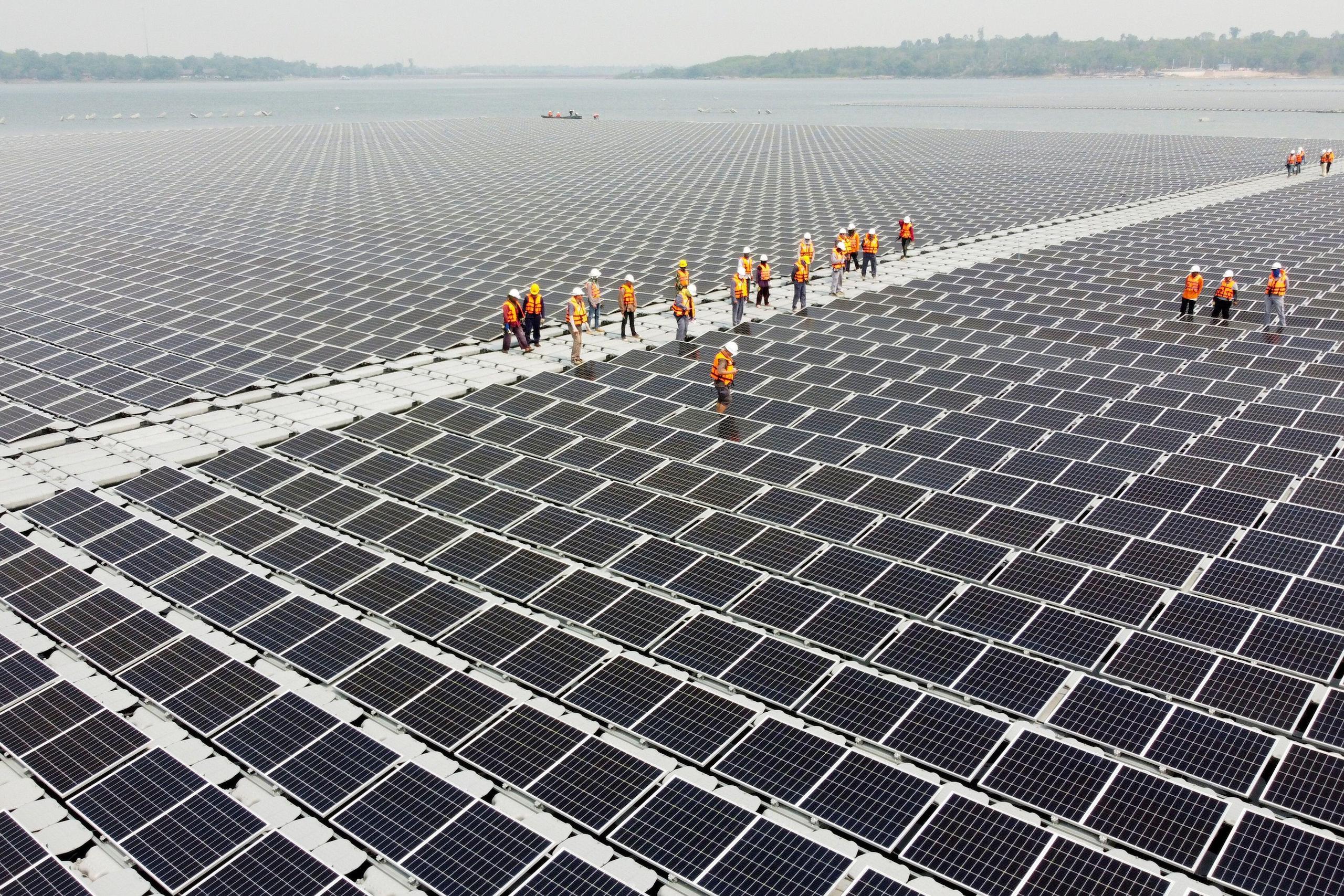 Workers walk between solar cell panels over the water surface of Sirindhorn Dam, Thailand