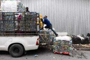 A <em>saleng</em> waste collector waits to be paid for a delivery of recyclable materials outside a recycling centre in Bangkok. The compressed plastic bottles in the background were all collected by workers like him, and will be sold on in bulk to make new bottles. (Image: Luke Duggleby / China Dialogue)