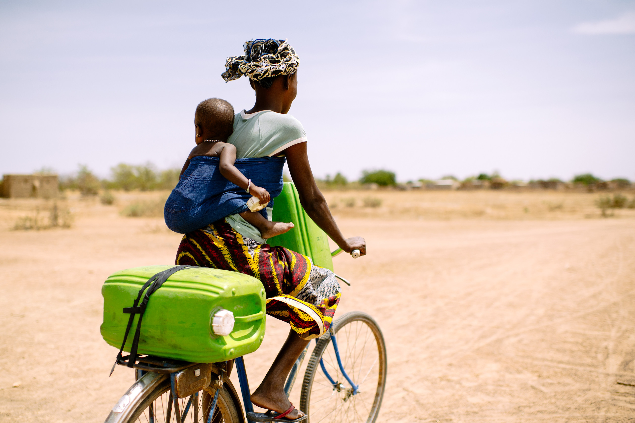 A woman rides her bicycle with her baby to collect water for her family, Sorobouly village near Boromo, Burkina Faso.