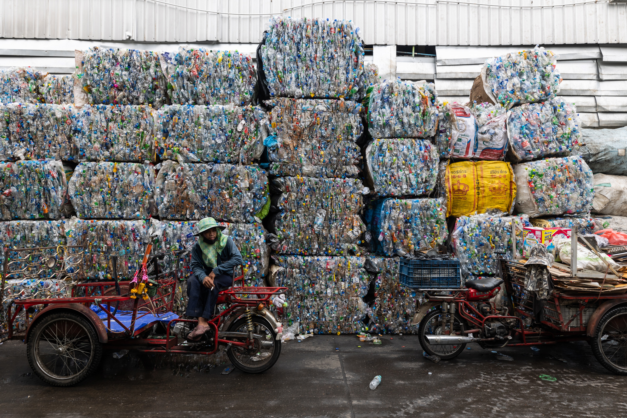 A saleng driver waits outside a large recycling plant in central Bangkok infant of large bricks of compressed plastic bottles.