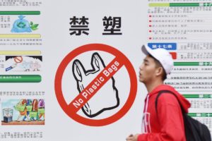 University student walks past a poster banning plastic bags in Haikou, China