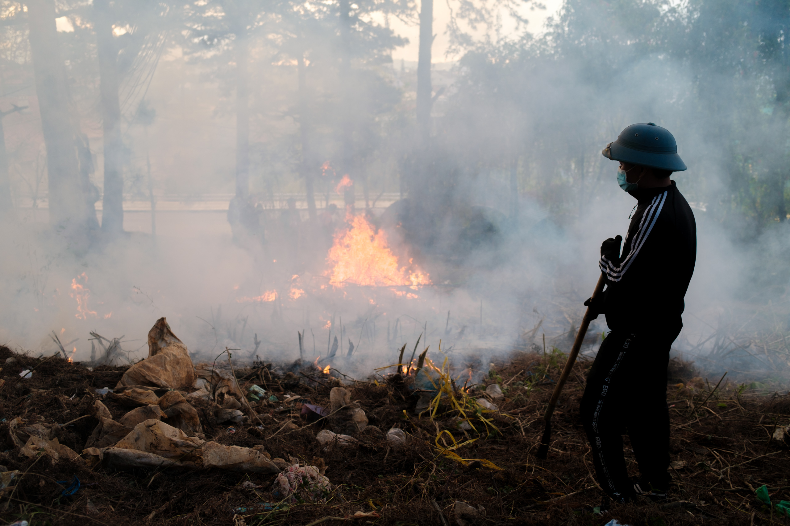 Silhouetted Vietnamese man burning waste surrounded by smoke