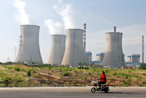 A Chinese woman rides her electric bike past a coal-fired power plant in Huaian city,