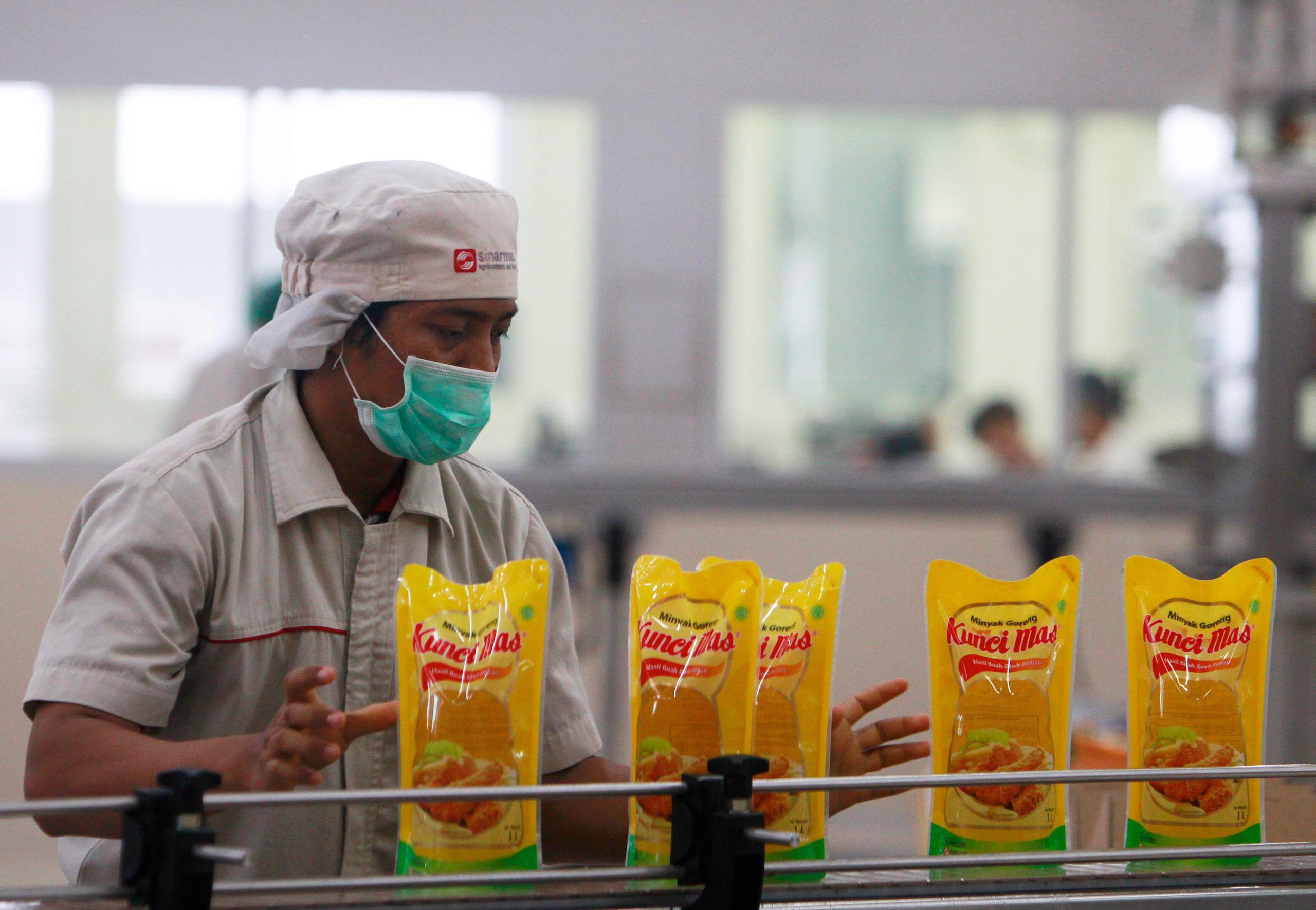 Man wearing a face mask moves yellow packets of cooking oil from a conveyor belt