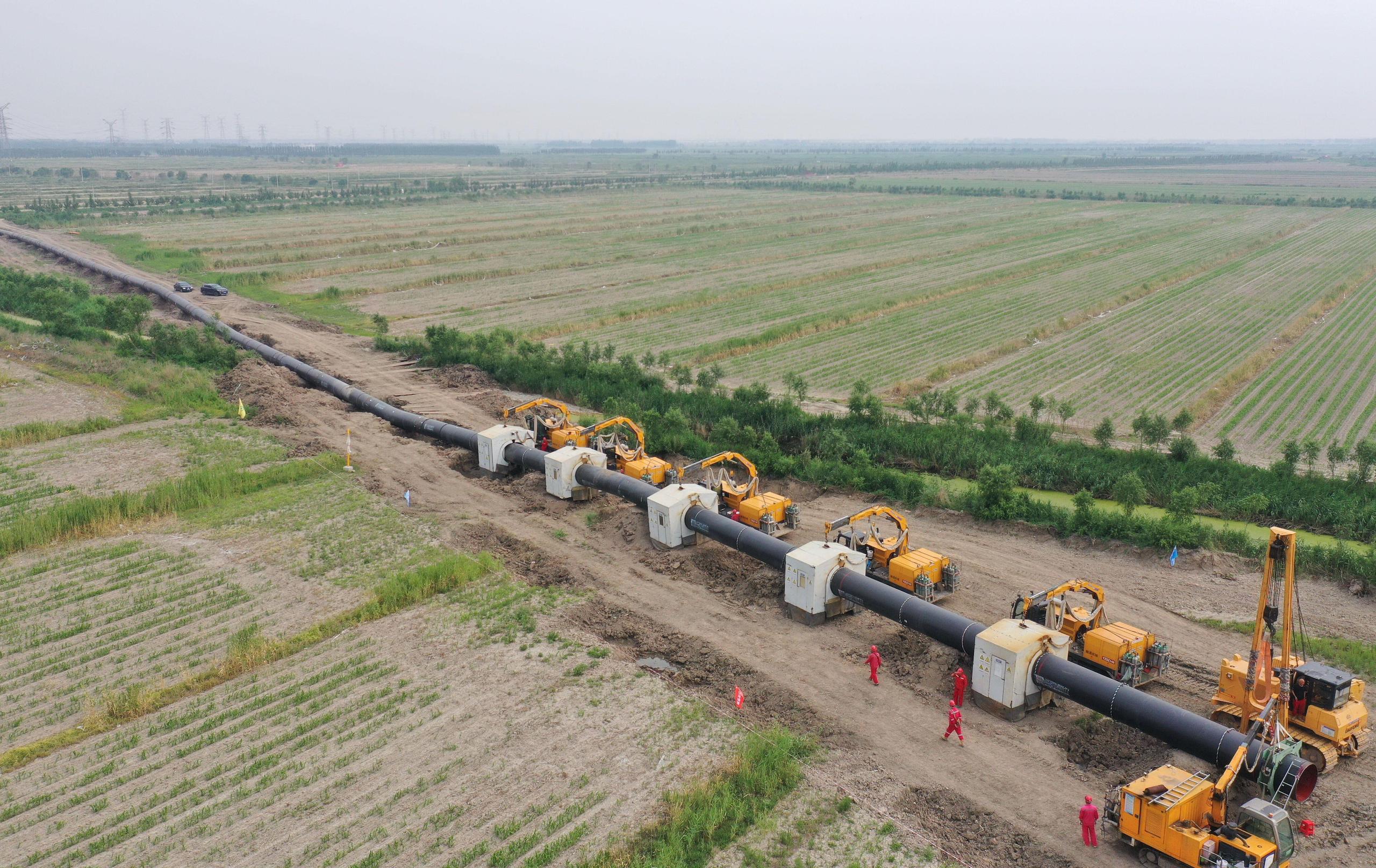 Aerial photo of workers installing pipe sections at a construction site for the outbound pipeline of a liquefied natural gas (LNG) receiving station in rural China