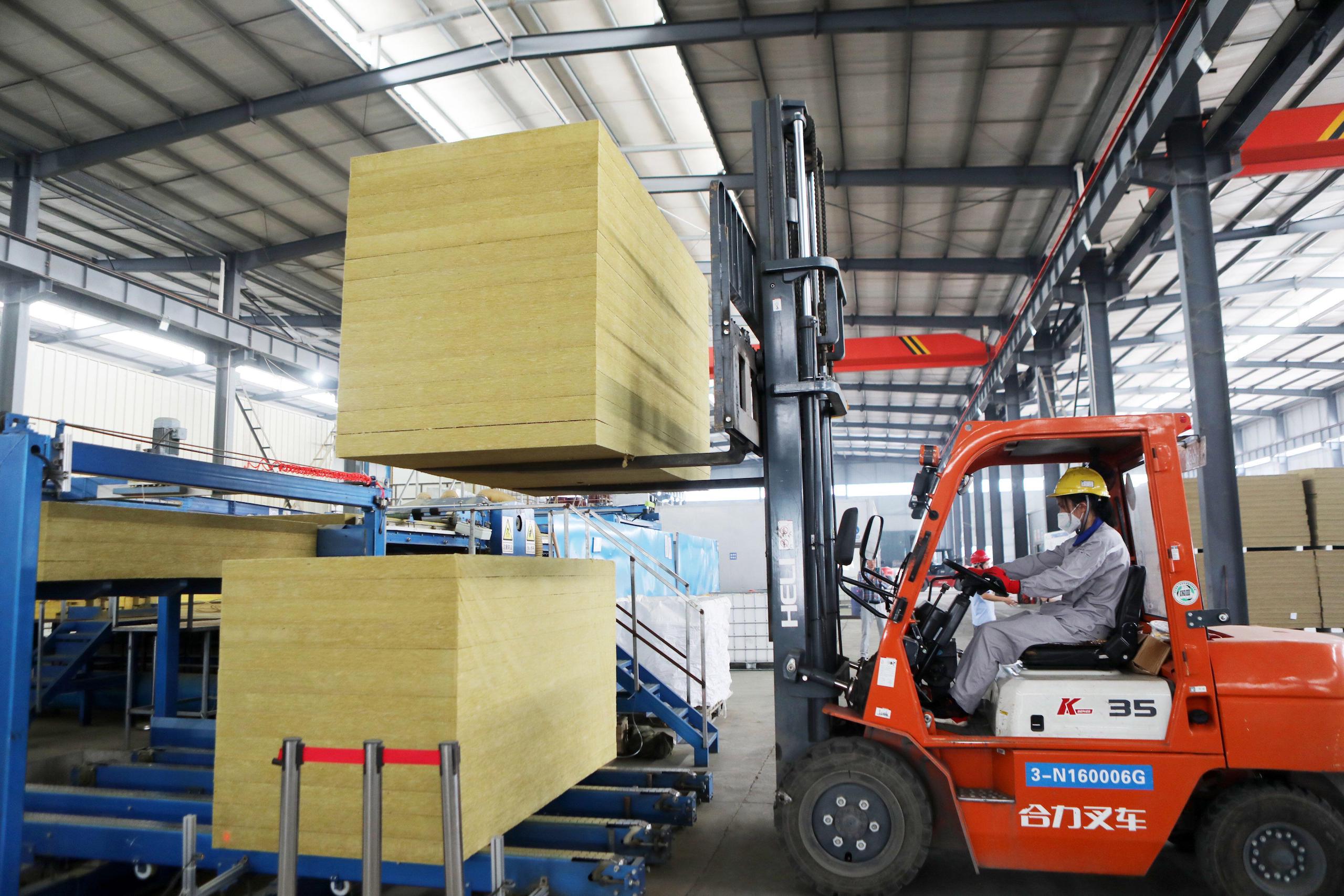 A red forklift holding up a block of stacked yellow insulation material, on a factory floor in Chongqing China, construction and housing sector China