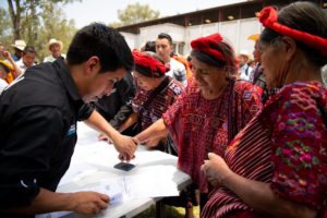 man helps woman in colourful clothing press thumb on ink pad in election Guatemala