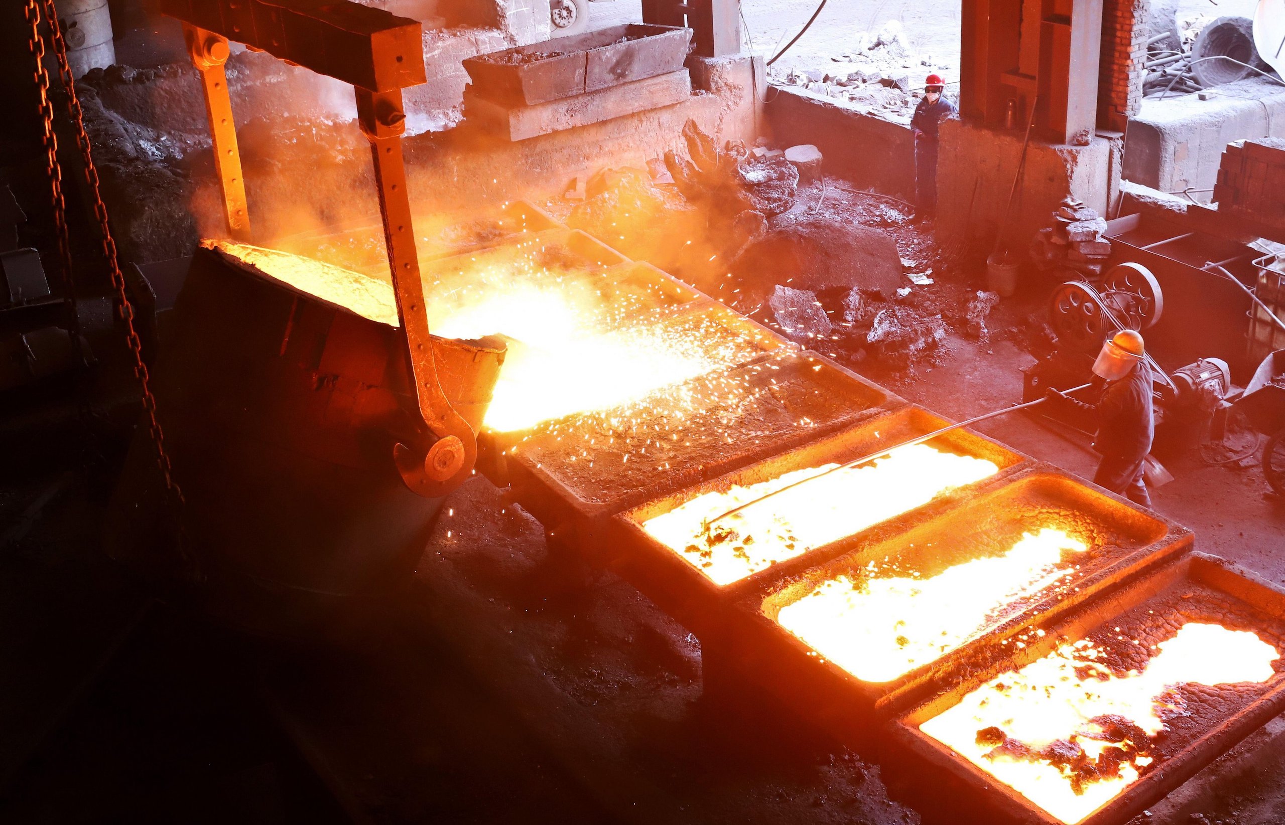 Person wearing protective clothing next to large tubs of bright yellow molten metal