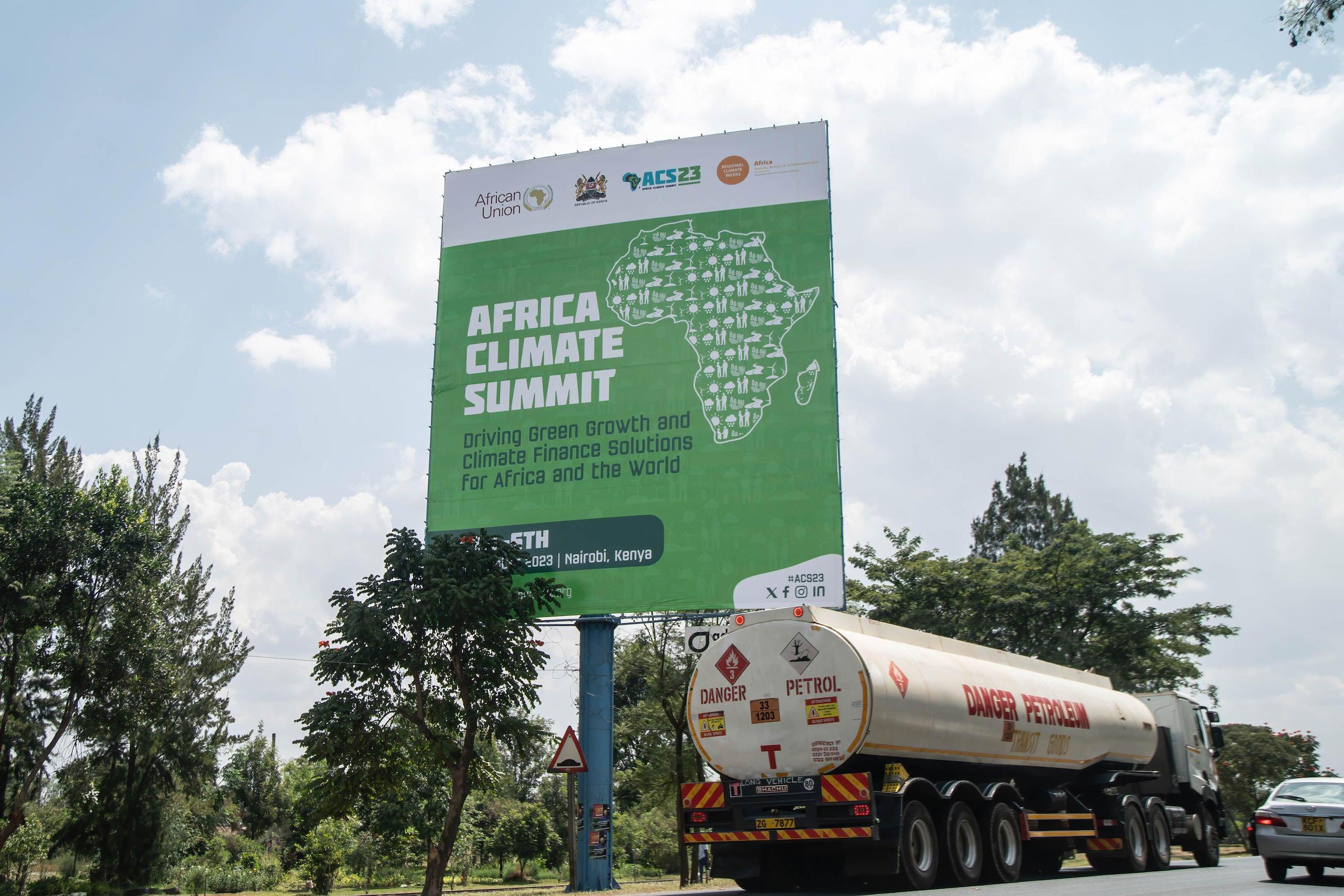 An oil tanker truck drives past a sign advertising the Africa Climate Summit