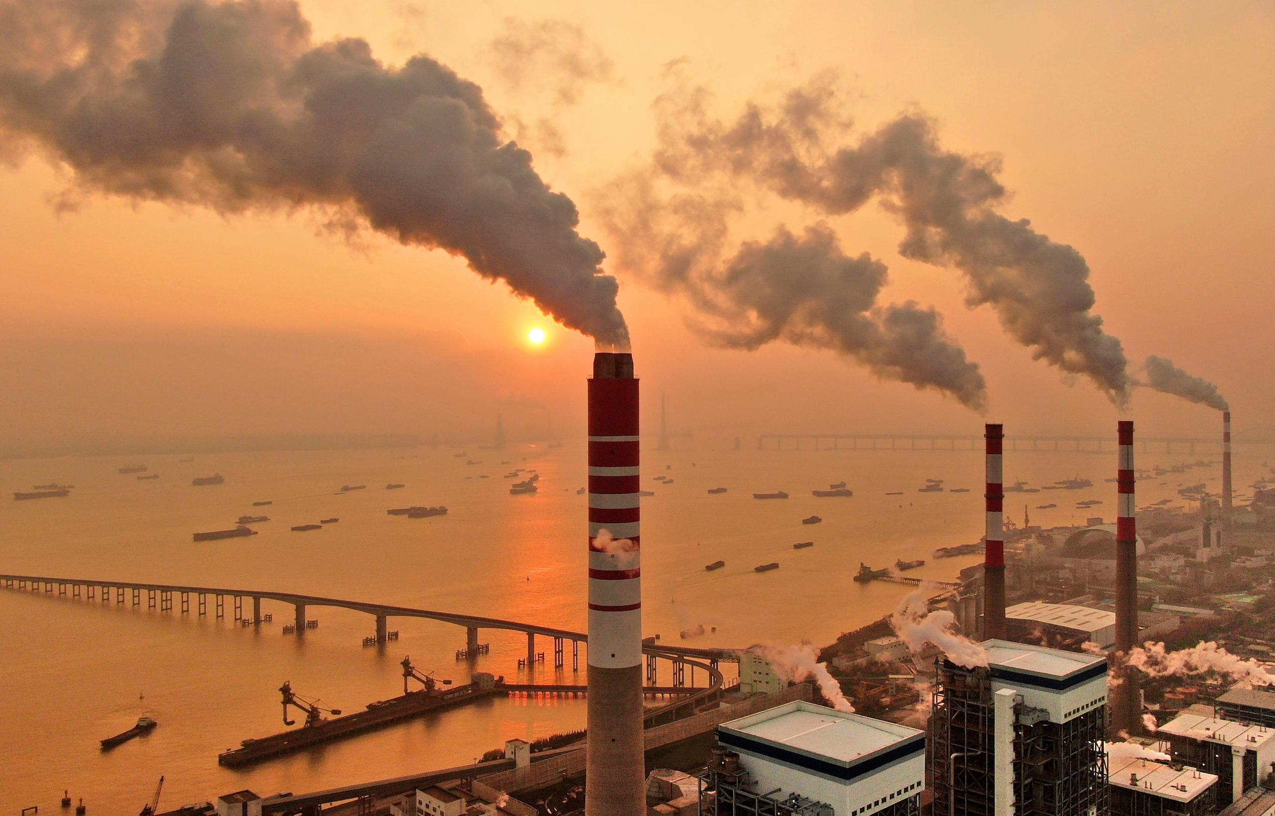 Smokestacks in front of a sunset over a busy port town